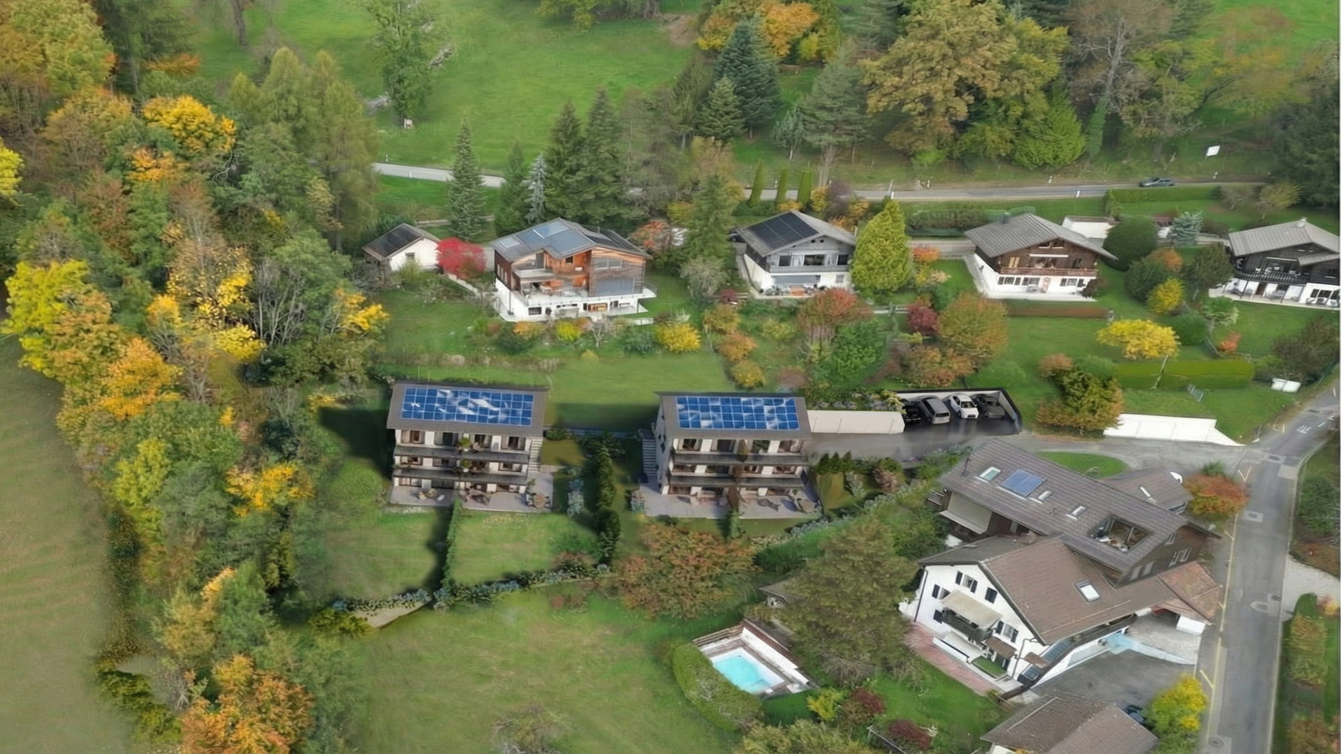 Vue aérienne d’un petit ensemble résidentiel de deux immeubles neufs à toits équipés de panneaux solaires, entourés de jardins, d’arbres et de villas voisines.